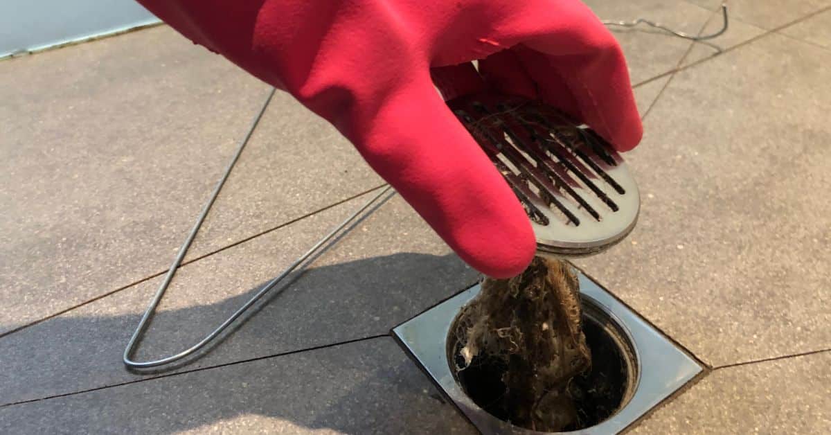 drainage service near me - Person lifting up a shower drain filled with hair