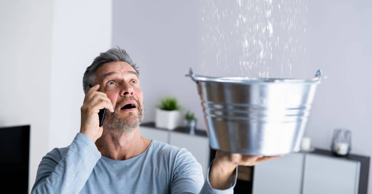 plumber South West London - Man holding up a bucket because his sealing is leaking water and is on the phone