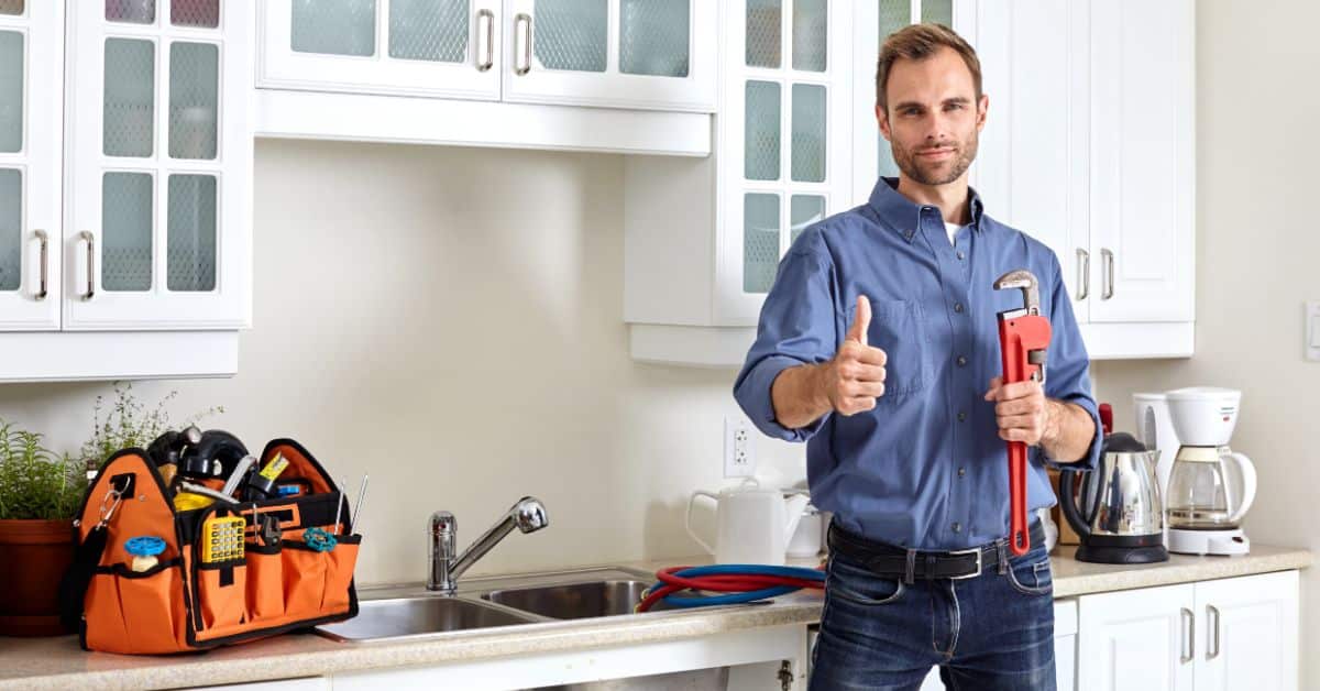 General plumber standing at a kitchen sink with his thumb up and plumbing gear on the side