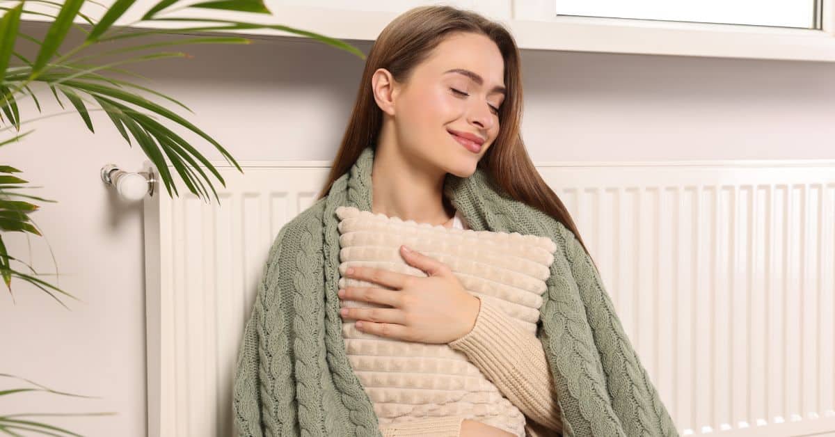 Lady sitting against a radiator with her blanket and cushion 