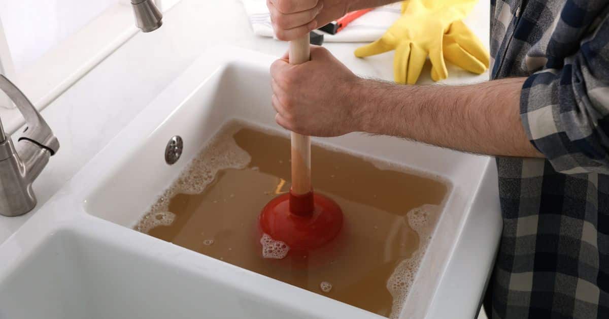 drains services - man using a plunger to unblock sink