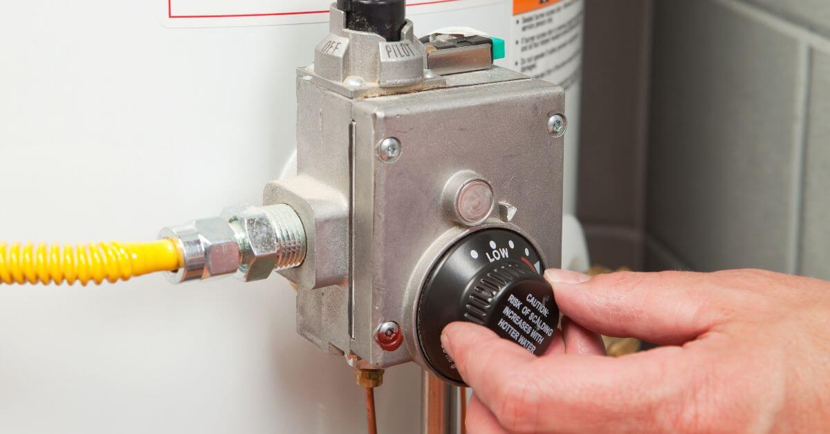 Man turning a water heater thermostat gauge
