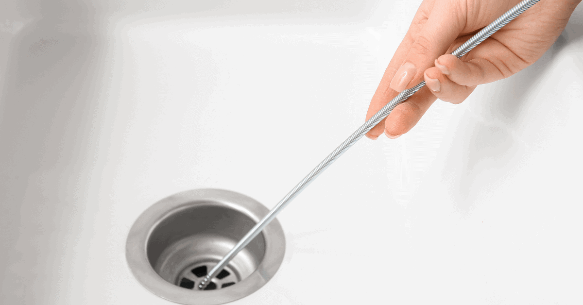 Homeowner using a Drain snake to loosen hair buildup in drain pipe 