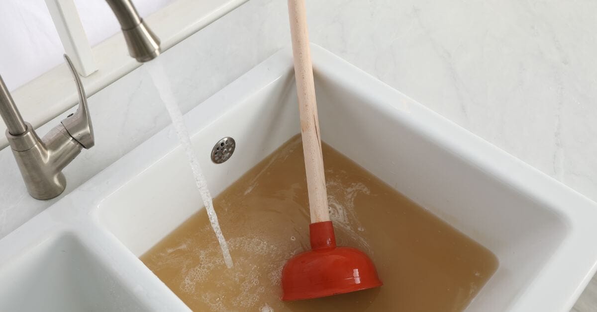 Water running into a blocked sink with brown water and a plunger